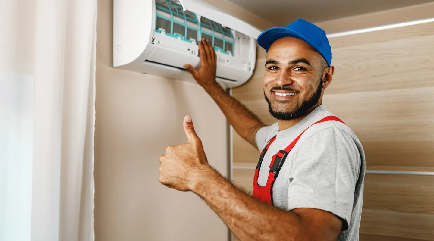 An engineer giving a thumbs up beside a wall-mounted air conditioning unit