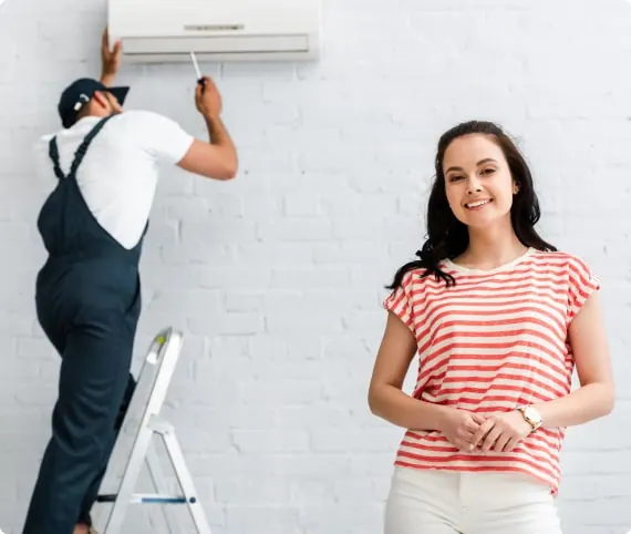 An engineer on a ladder working on an indoor air conditioning unit