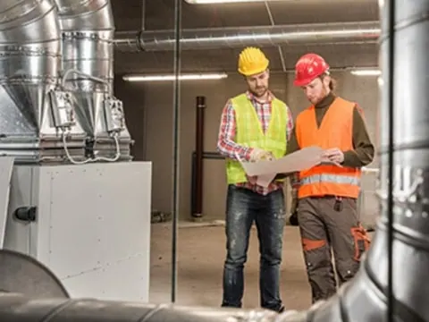 Two engineers in hard hats reviewing plans in a plant room