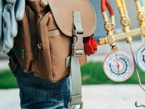 An engineer carrying refrigerant manifold gauges and a tool bag