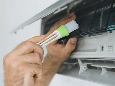 An engineer cleaning the filter of an air conditioning unit with a brush